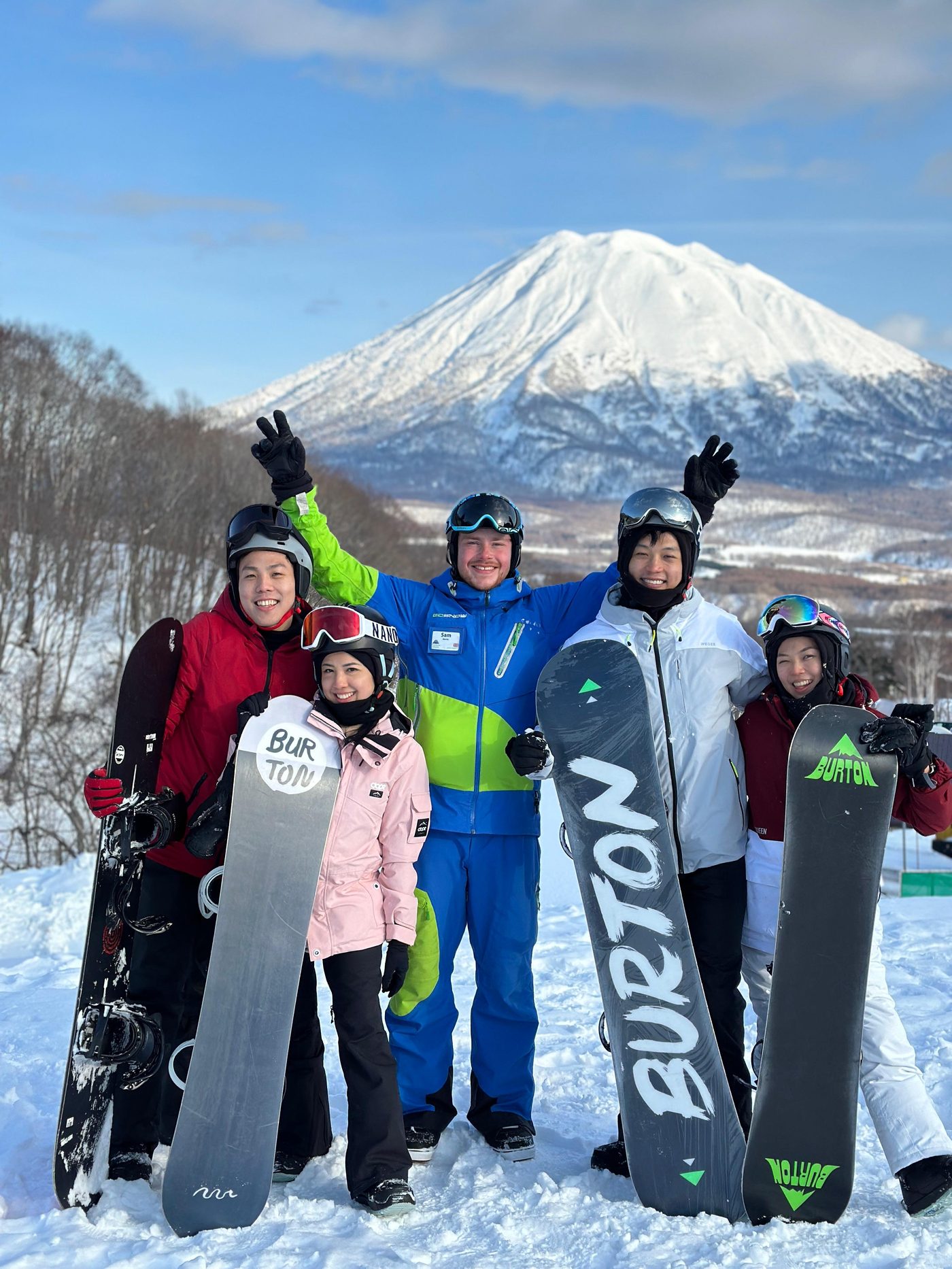 Sam Martin in his GoSnow instructor uniform with five clients holding snowboards, Mount Yotei behind them